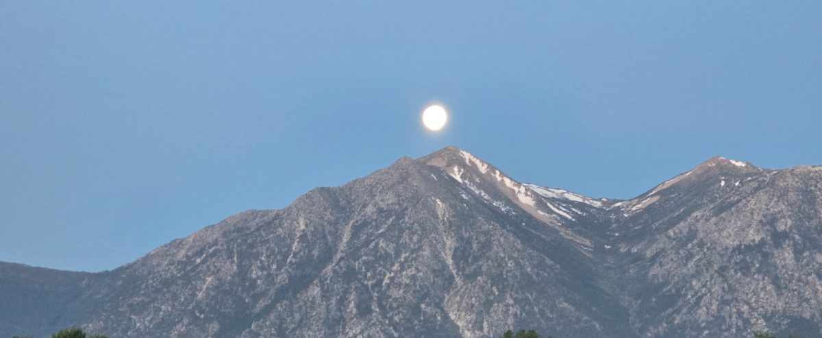 A full moon rising over snow-streaked Sierra Nevada peaks at dusk
